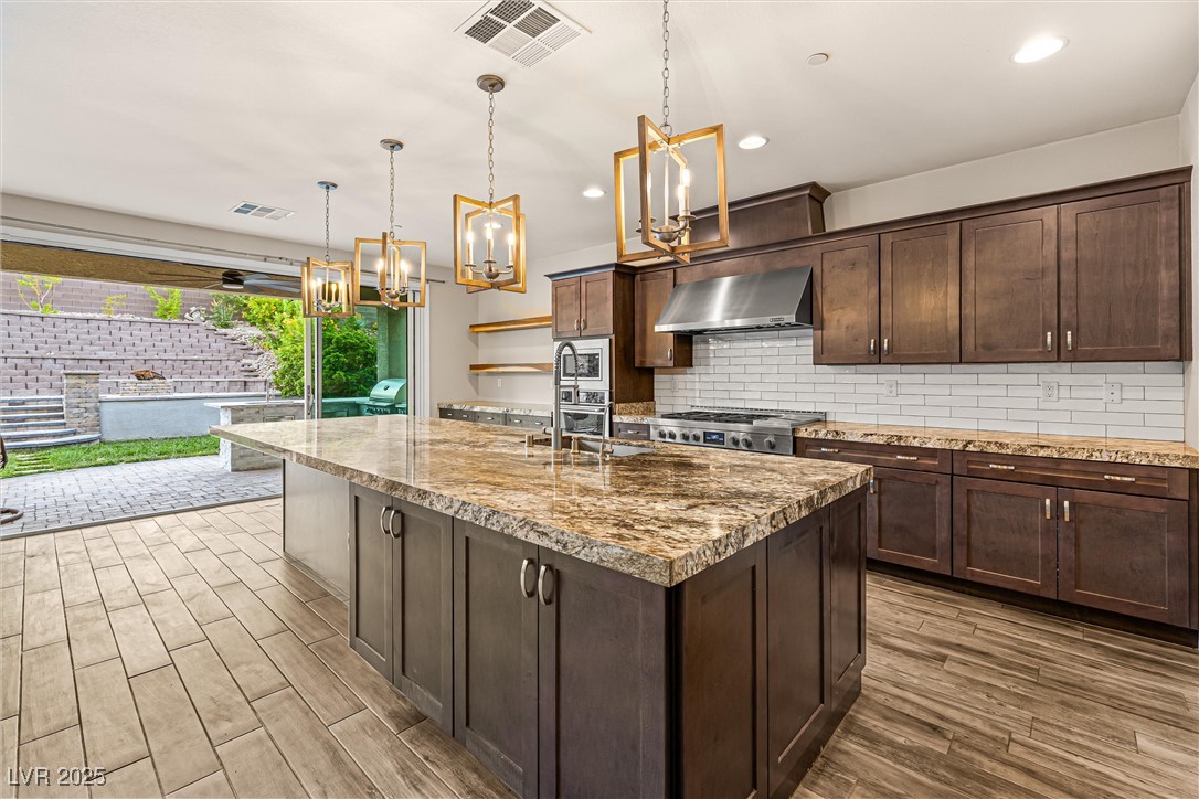 4631 Amazing View Street Las Vegas, NV 89129 - Photo 18 of 94 Kitchen featuring dark brown cabinets, tasteful backsplash, light stone countertops, wall chimney exhaust hood, and pendant lighting