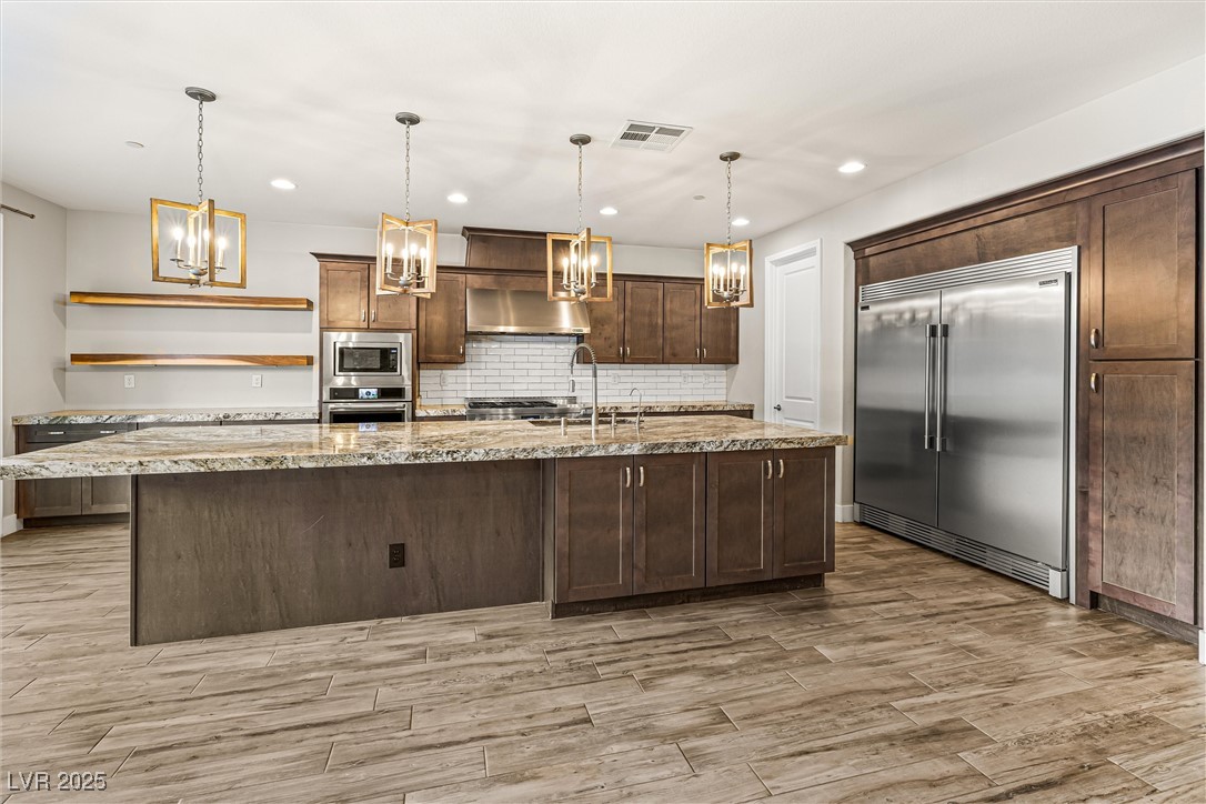 4631 Amazing View Street Las Vegas, NV 89129 - Photo 19 of 94 Kitchen featuring decorative backsplash, built in appliances, a large island with sink, open shelves, and light stone countertops