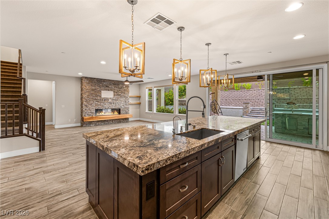 4631 Amazing View Street Las Vegas, NV 89129 - Photo 21 of 94 Kitchen featuring dark brown cabinets, a stone fireplace, wood tiled floors, recessed lighting, and an island with sink