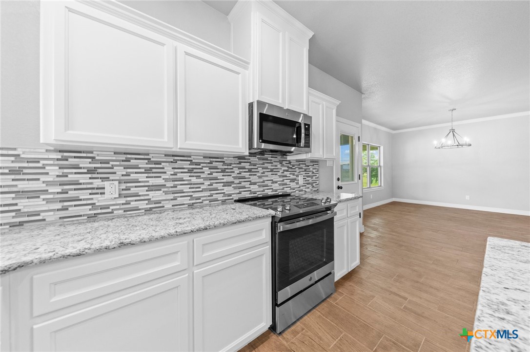 3030 Millhouse Road Copperas Cove, TX 76522 - Photo 4 of 24 a kitchen with granite countertop a sink dishwasher a stove and a microwave oven with wooden floor