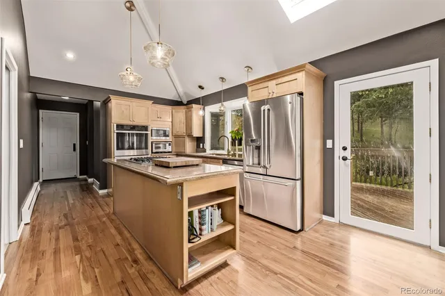 a kitchen with stainless steel appliances granite countertop a refrigerator a sink dishwasher a stove and a dining table with wooden floor