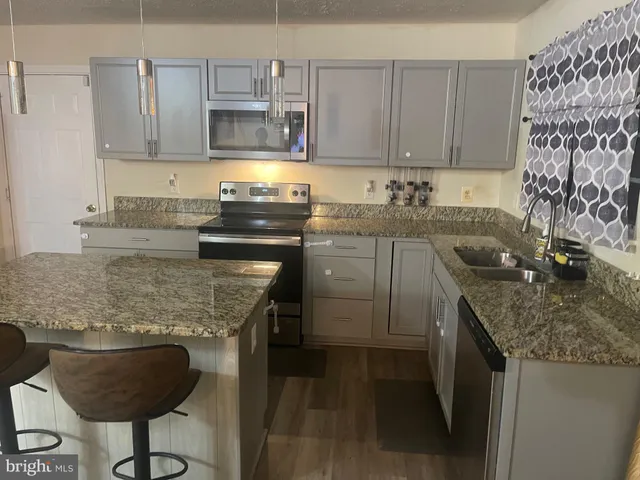 a kitchen with granite countertop kitchen island stainless steel appliances a sink stove and cabinets