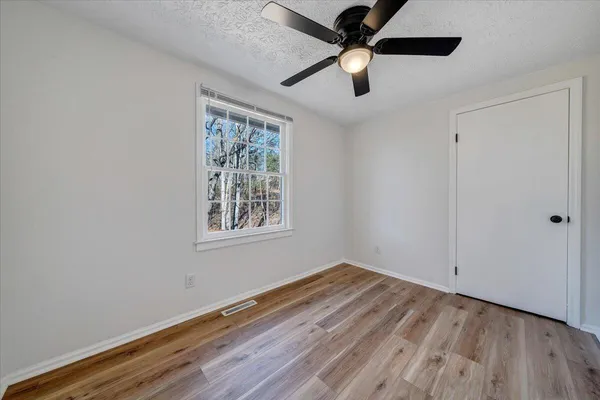 an empty room with wooden floor ceiling fan and windows