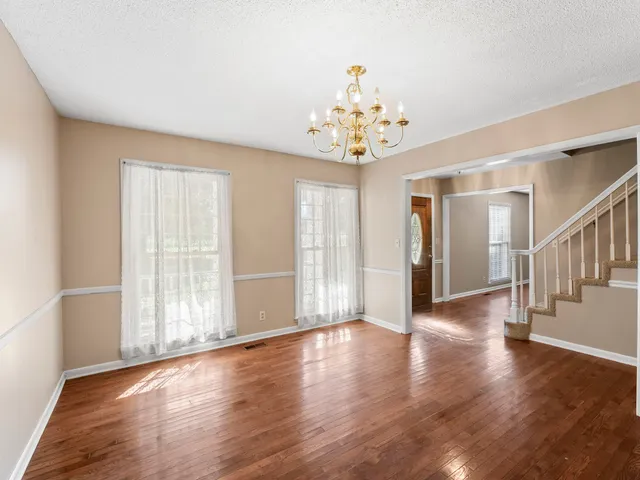 a view of an empty room with chandelier fan and wooden floor