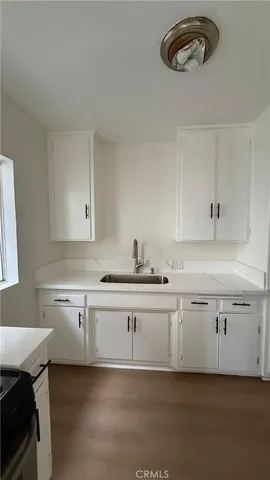 a white kitchen with a sink and dishwasher a stove top oven with wooden floor