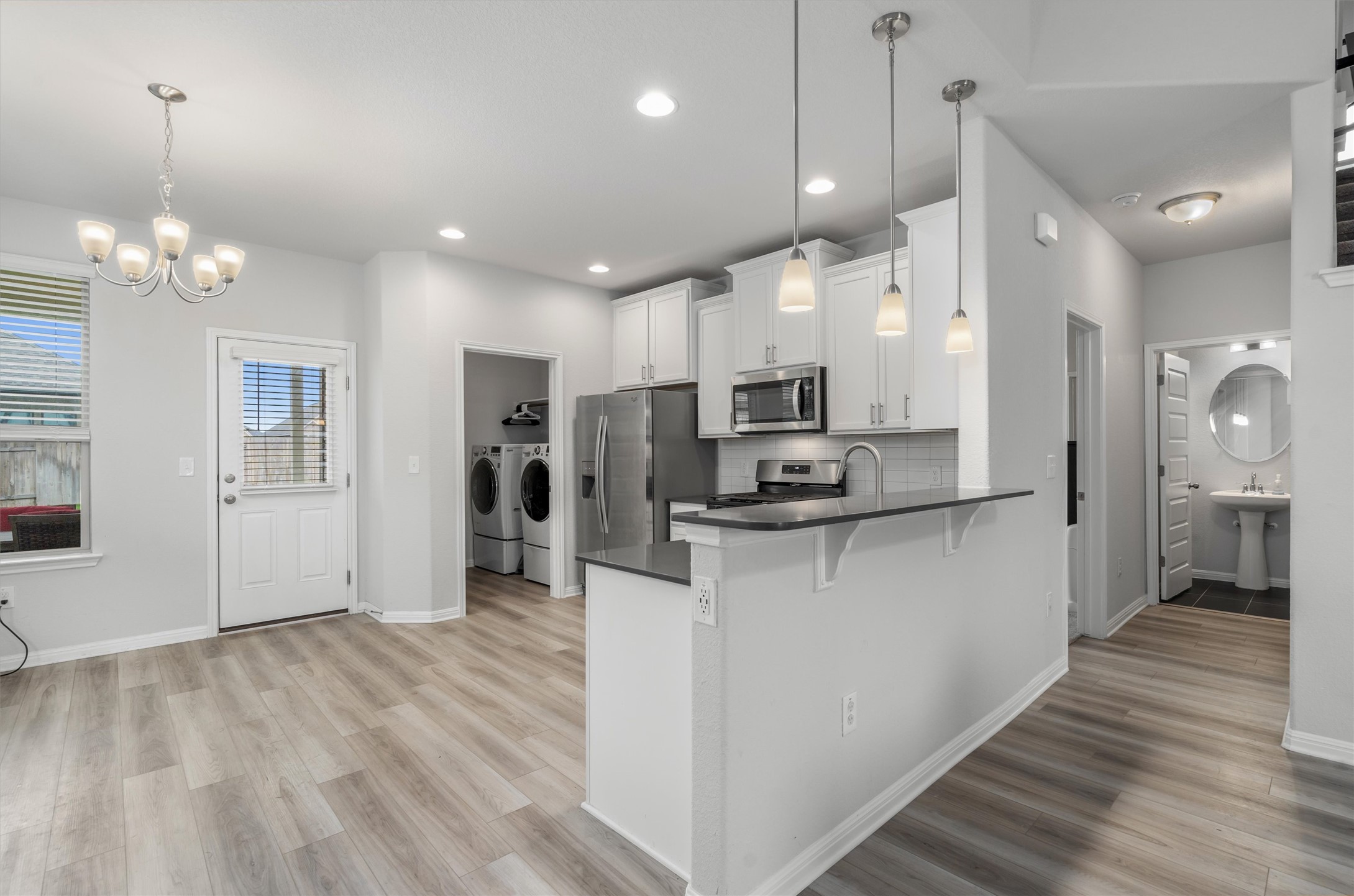 224 Backstays Loop Kyle, TX 78640 - Photo 7 of 19 Open concept living space featuring wood-finish flooring, a white kitchen with stainless steel appliances, pendant lighting, and an integrated kitchen island with a breakfast bar