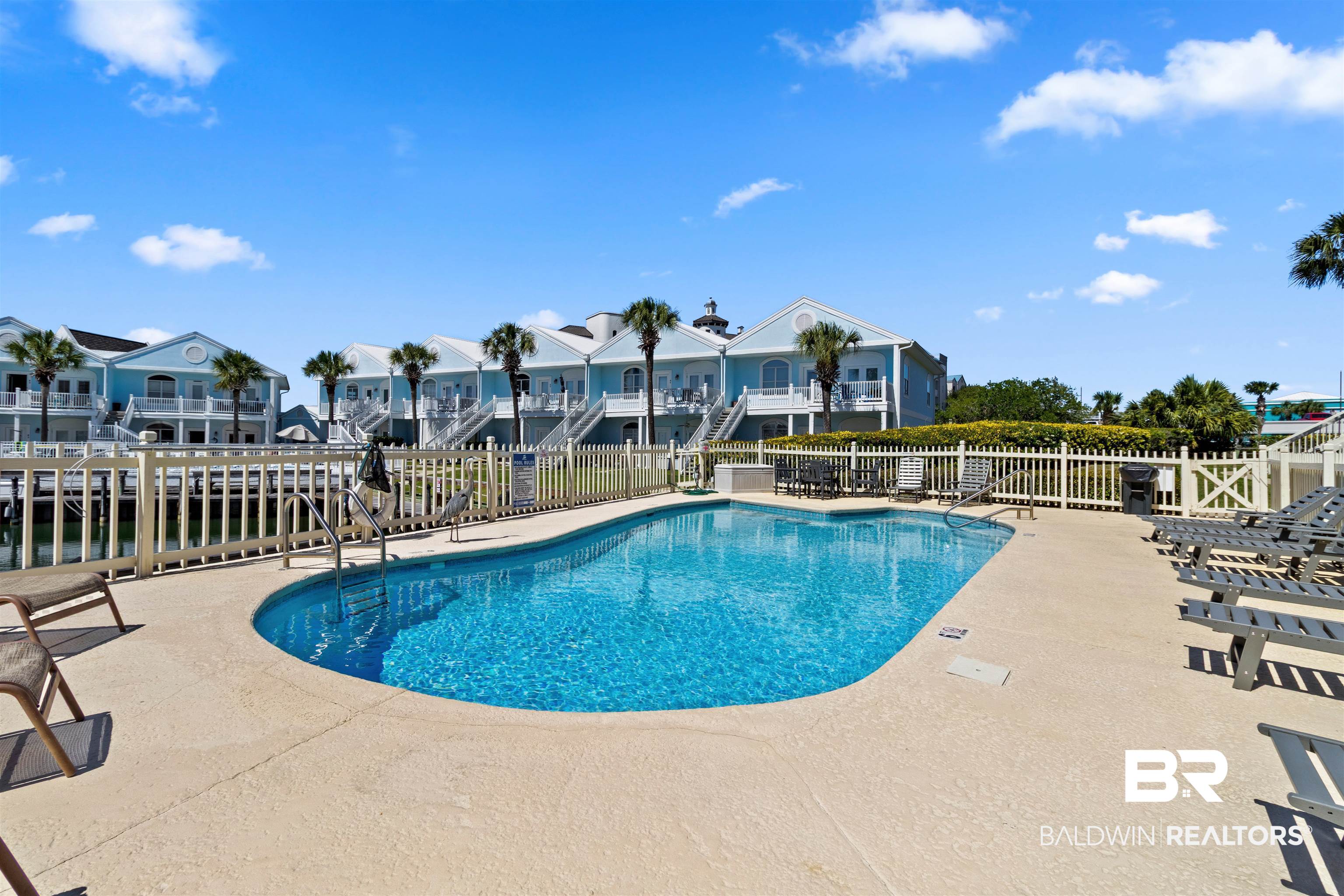 3543 Bayou Road, Unit 5 Orange Beach, AL 36561 - Photo 18 of 33 Resort-style swimming pool with surrounding patio, white picket fencing, and palm trees