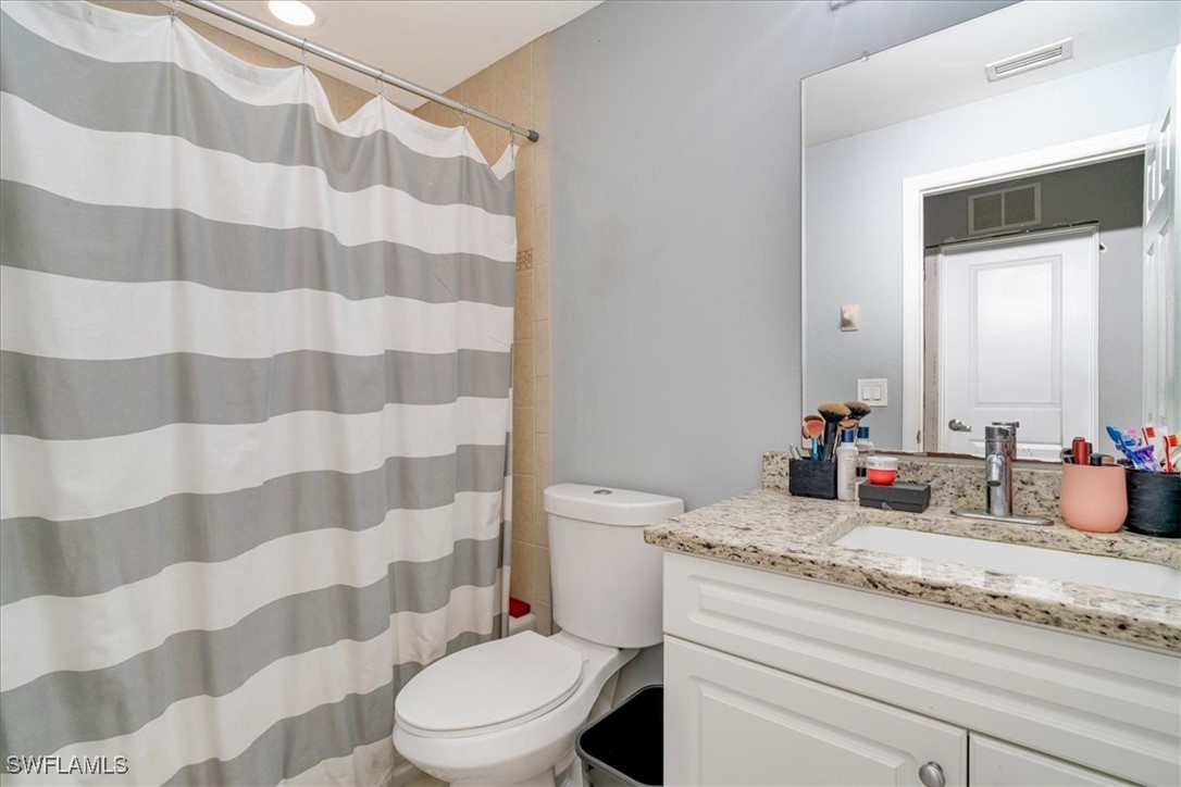 3980 Sunset Road Lehigh Acres, FL 33971 - Photo 30 of 42 a bathroom with a granite countertop sink a toilet a mirror and shower curtain