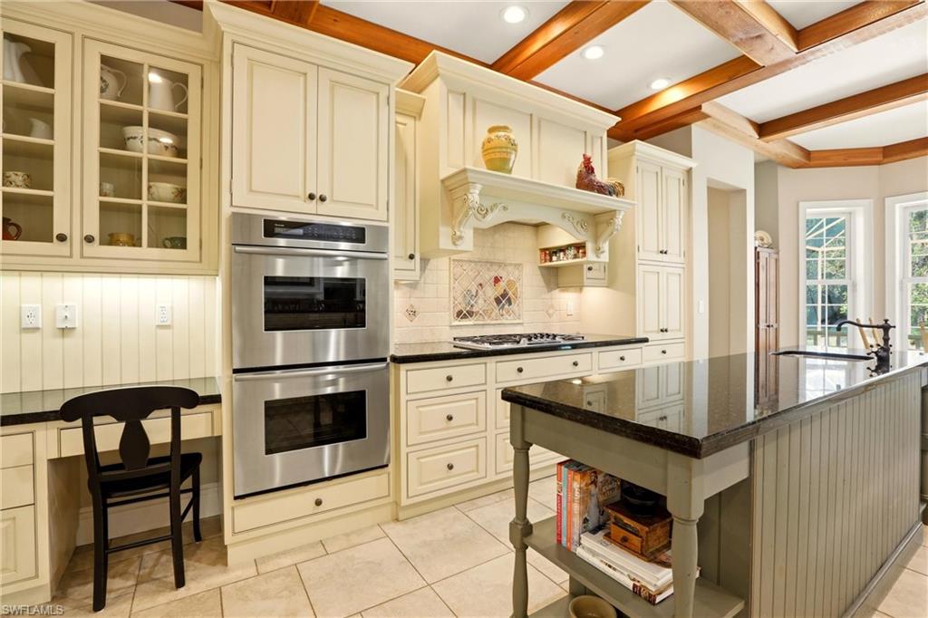4335 7th Avenue Southwest Naples, FL 34119 - Photo 12 of 49 Kitchen with open shelves, stainless steel appliances, glass insert cabinets, cream cabinets, and an island with sink