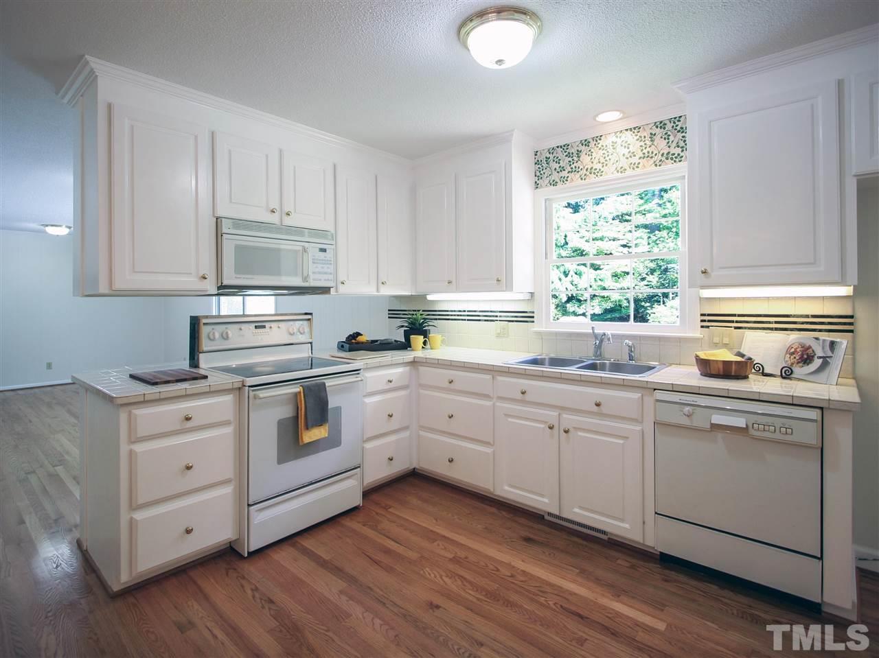 1324 Kingston Ridge Road Cary, NC 27511 - Photo 5 of 30 White cabinets and newly-refinished hardwood floors give this kitchen a bright and cheery look. You'll even enjoy washing the dishes with the lovely garden view from the window over the sink.