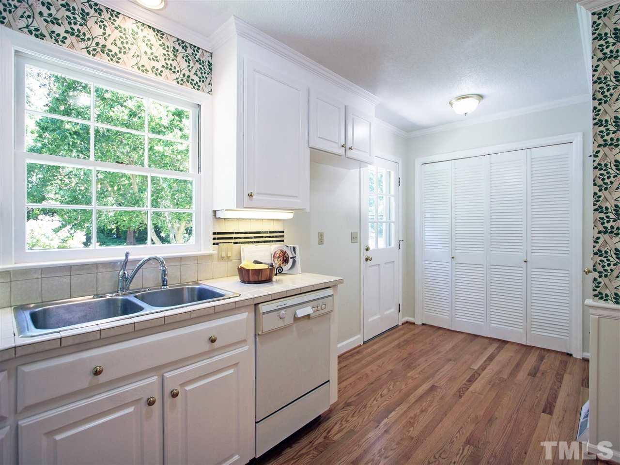 1324 Kingston Ridge Road Cary, NC 27511 - Photo 6 of 30 Kitchen has tile countertops and stainless steel sink. Built-in dishwasher. Louvered doors at the center of the photo are the laundry. Door shown at the left of the laundry leads to the backyard. Door to the right of the laundry leads to the garage.