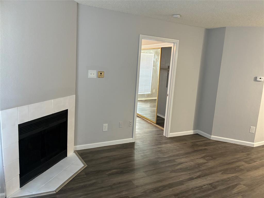 Unfurnished living room featuring dark wood-type flooring, a tiled fireplace, and a textured ceiling