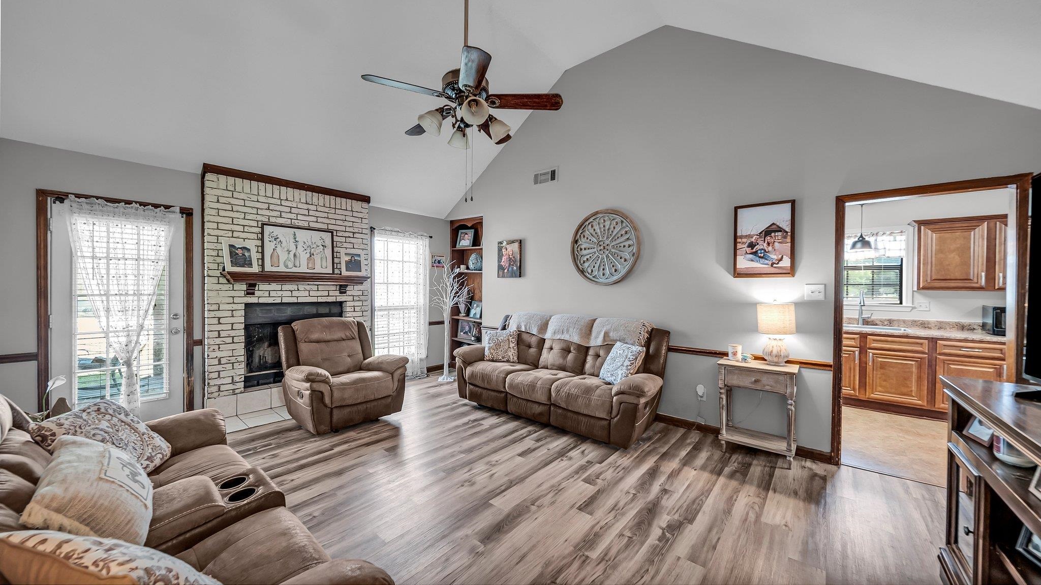 6488 Chase Road Millington, TN 38053 - Photo 7 of 22 Living room featuring high vaulted ceiling, a ceiling fan, a brick fireplace, light wood-style flooring, and visible vents
