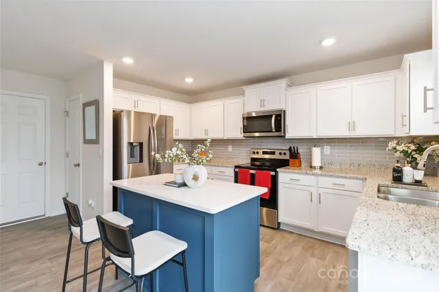 a kitchen with a sink a stove a refrigerator and white cabinets with wooden floor