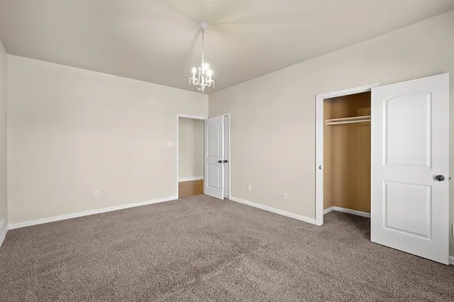 an empty room with chandelier fan and kitchen view