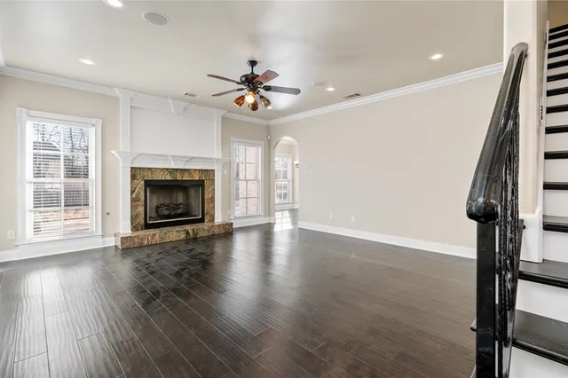 a view of an empty room with a fireplace a ceiling fan and wooden floor