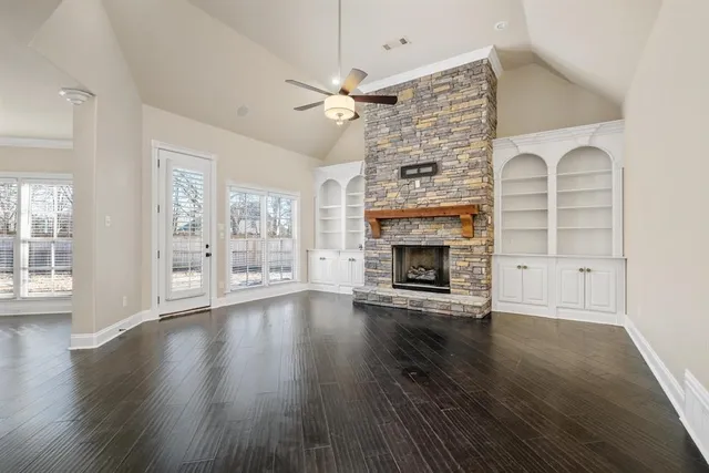 an empty room with wooden floor fireplace and windows