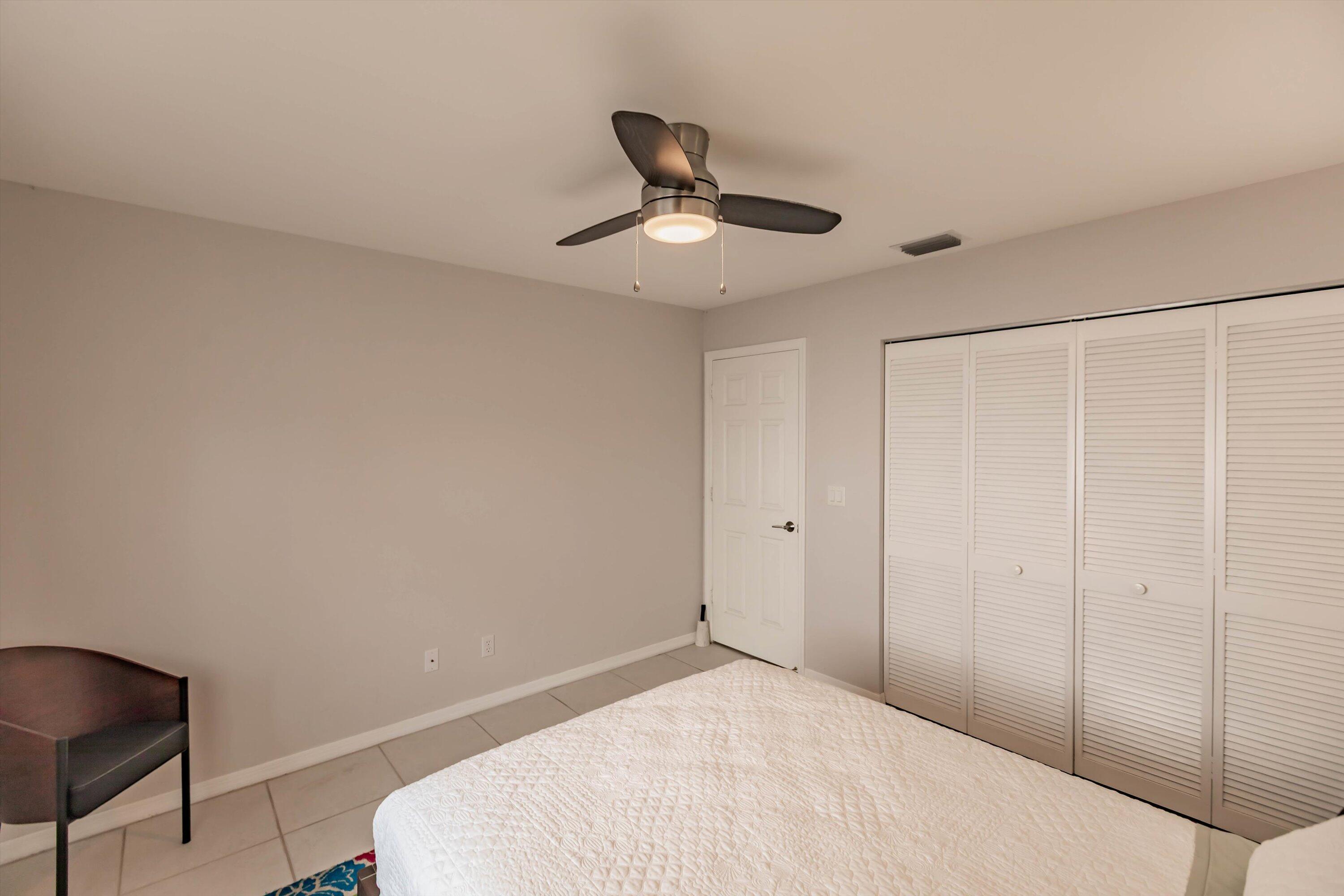 6115 Southeast Georgetown Place, Unit 1006 Hobe Sound, FL 33455 - Photo 25 of 68 a bedroom with a bed and a chandelier fan