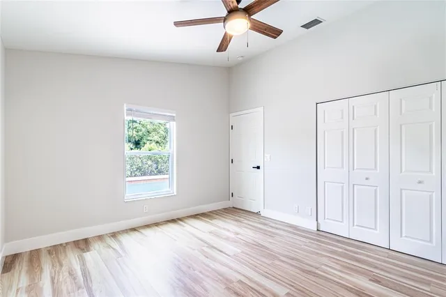 an empty room with wooden floor chandelier fan and windows