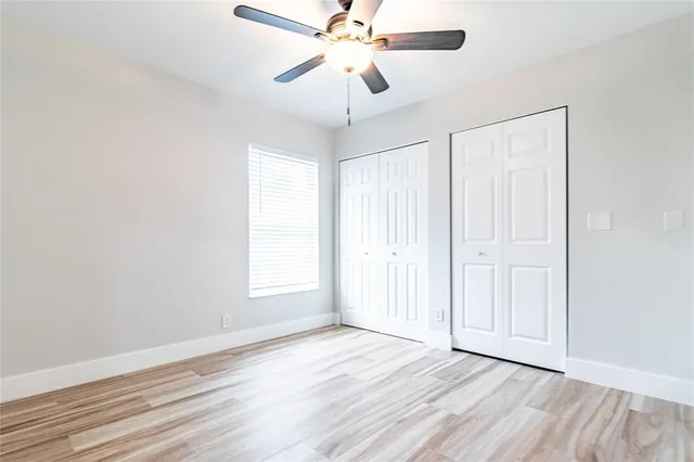 an empty room with wooden floor chandelier fan and windows