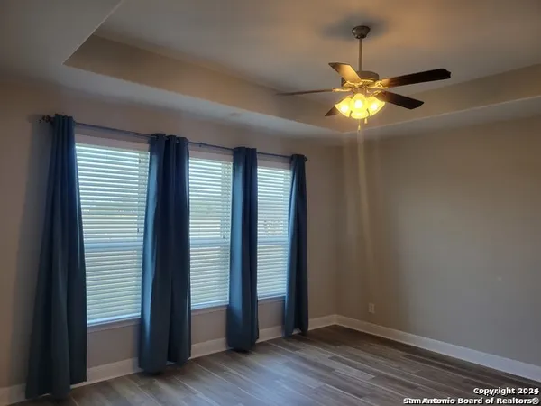 an empty room with wooden floor chandelier fan and windows