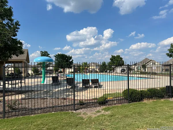 a view of a swimming pool with lawn chairs and a big yard with plants and palm trees