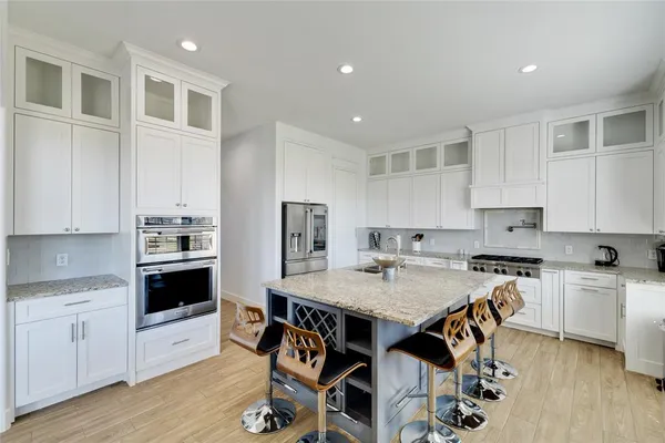 a kitchen with stainless steel appliances granite countertop a stove top oven a sink dishwasher and white cabinets with wooden floor