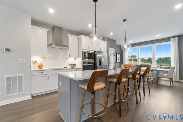 a kitchen with stainless steel appliances granite countertop a stove a refrigerator a kitchen island a dining table and chairs with wooden floor