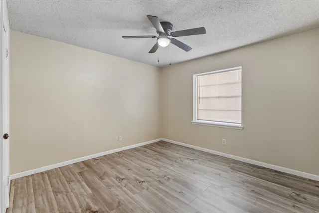 an empty room with wooden floor ceiling fan and windows