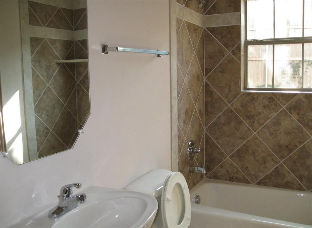 Bathroom featuring a ceramic tile shower surround, bathtub with shower fixture, wall-mounted sink, and an octagonal mirror