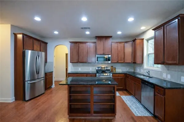 a kitchen with stainless steel appliances granite countertop a refrigerator a sink dishwasher a stove and a refrigerator with wooden floor
