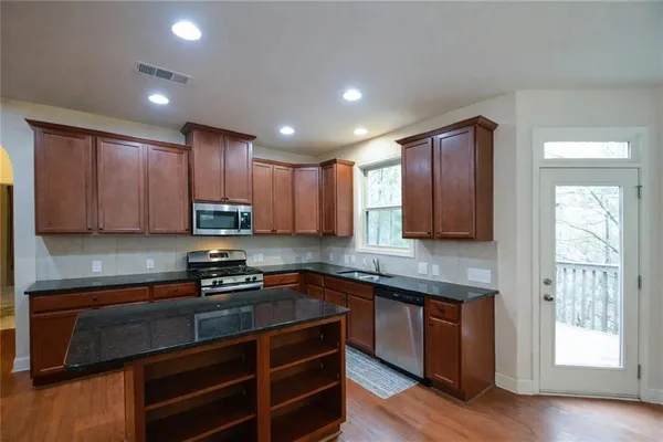 a kitchen with stainless steel appliances granite countertop wooden cabinets a stove top oven a sink and dishwasher with wooden floor