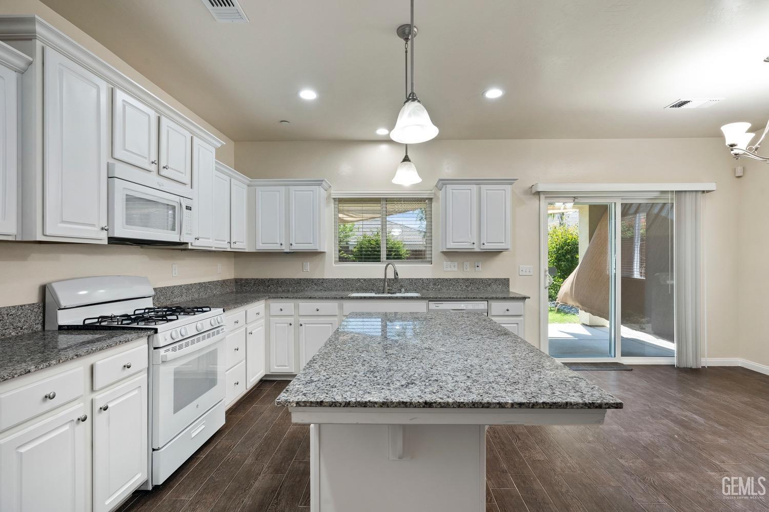 Undisclosed Address Bakersfield, CA 93311 - Photo 9 of 27 a kitchen with kitchen island granite countertop a stove a sink and white cabinets