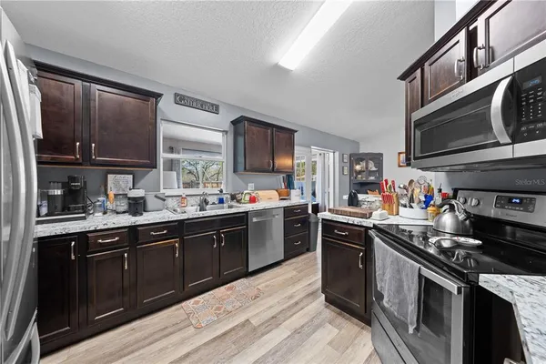 a kitchen with stainless steel appliances granite countertop a stove a sink dishwasher and a microwave oven with wooden cabinets