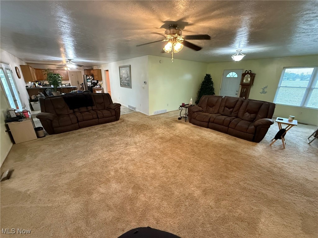 Living area featuring a ceiling fan, light colored carpet, and a textured ceiling