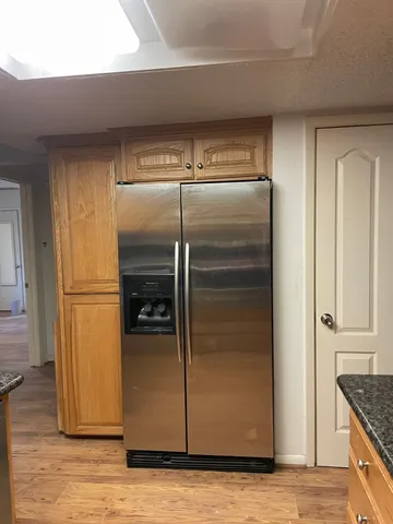 a view of a refrigerator in kitchen and an empty room with wooden floor