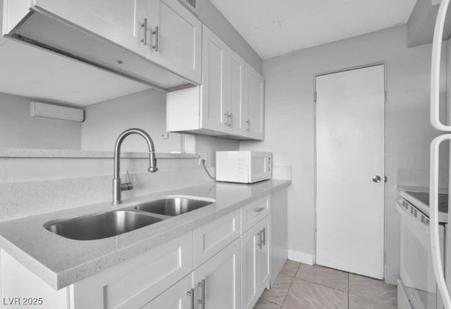 239 West Cleveland Avenue, Unit 2 Las Vegas, NV 89102 - Photo 5 of 13 Kitchen featuring white cabinets, white appliances, light tile patterned flooring, a wall unit AC, and light stone counters