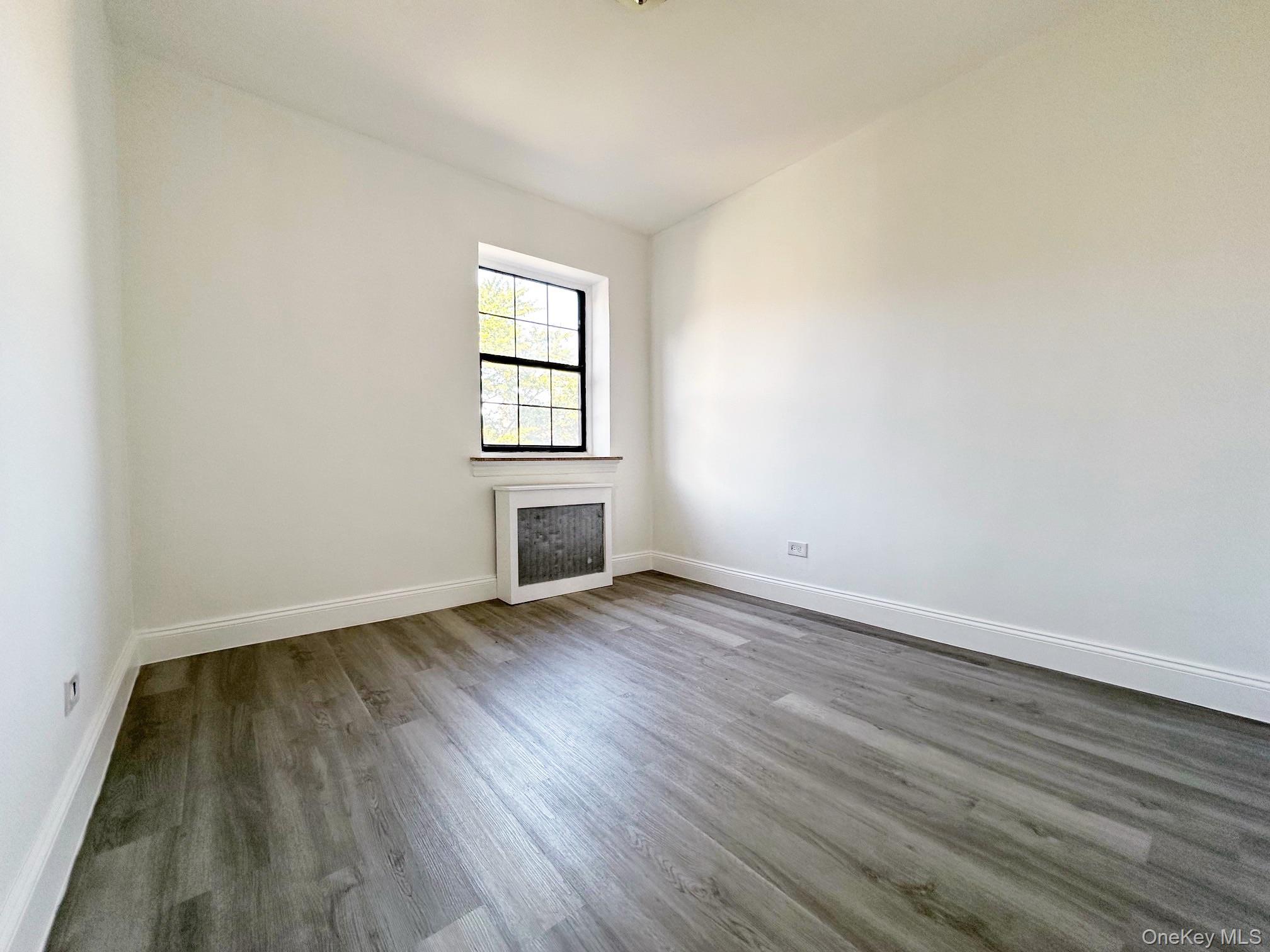 78-16 147th Street, Unit 3C Queens, NY 11367 - Photo 5 of 16 Empty room with wood finished floors and radiator heating unit