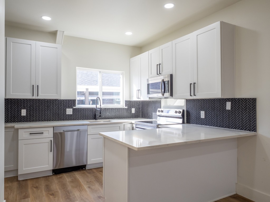 a kitchen with stainless steel appliances a sink a stove a refrigerator and white cabinets