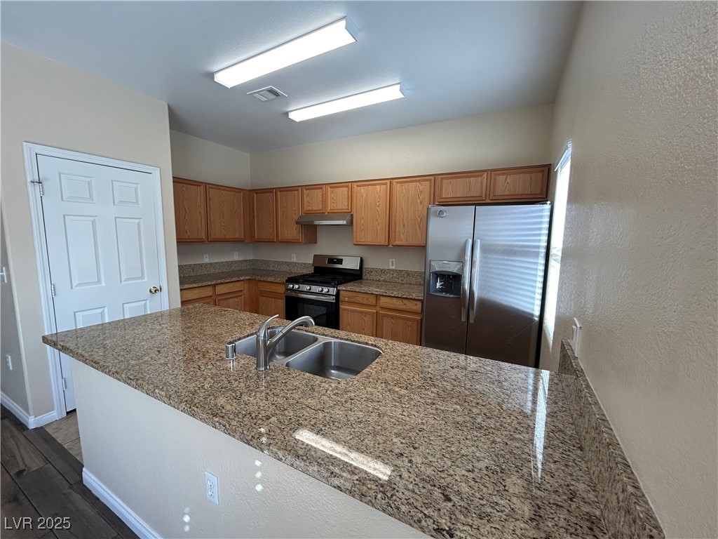 9303 Gilcrease Avenue, Unit 1131 Las Vegas, NV 89149 - Photo 3 of 36 Kitchen with stainless steel appliances, brown cabinets, dark stone counters, a peninsula, and a textured wall