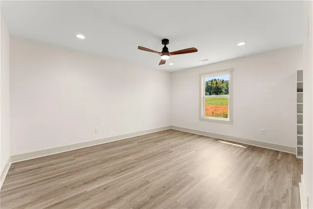 an empty room with wooden floor ceiling fan and window