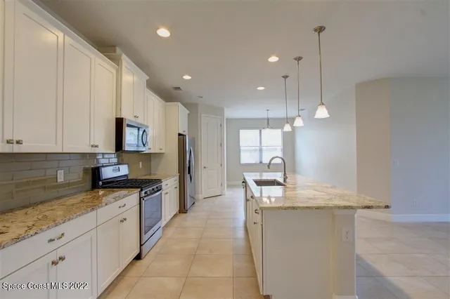 a large kitchen with granite countertop a sink a counter top space appliances and cabinets