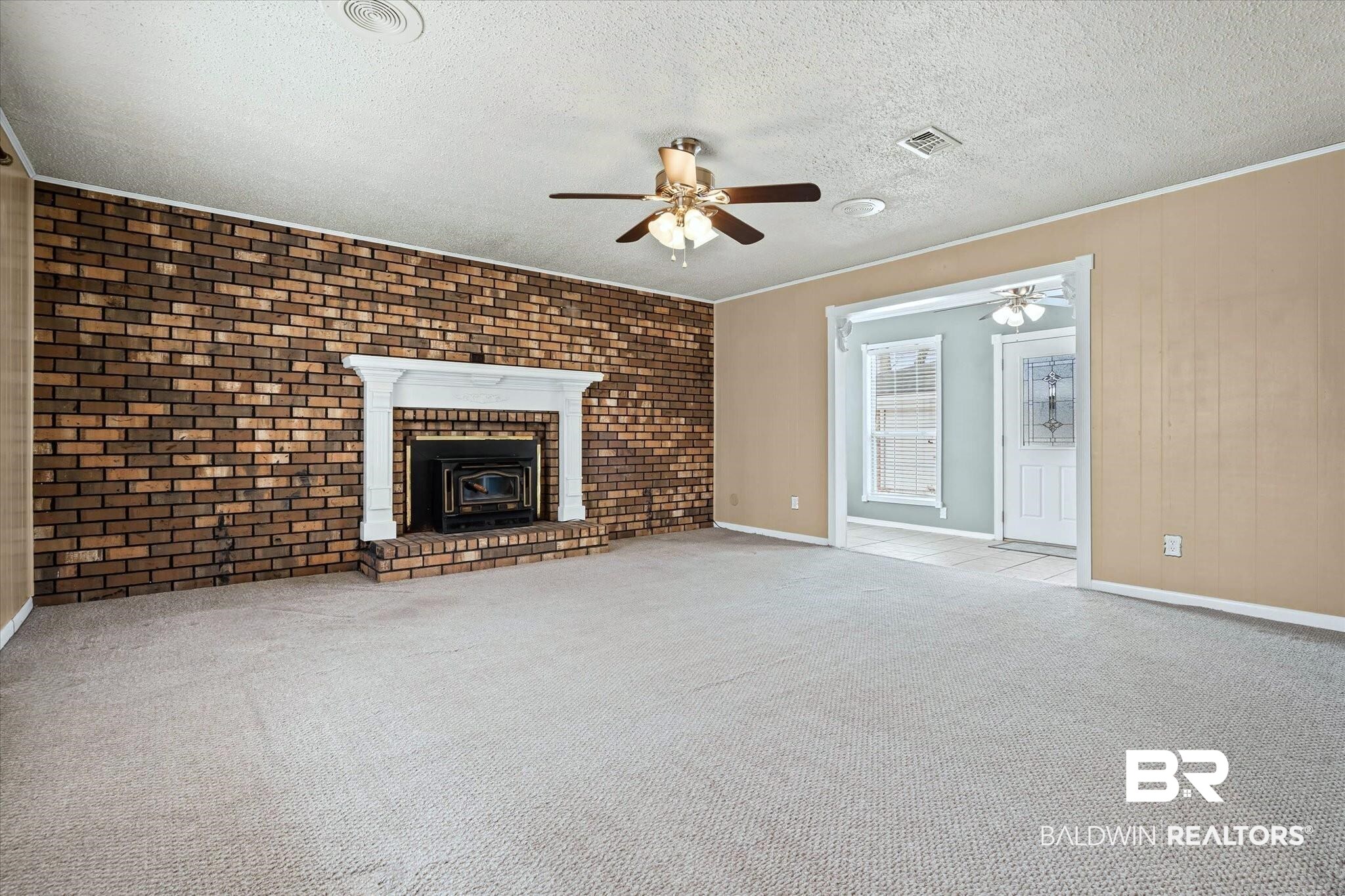 8090 Murray Hill Road Irvington, AL 36544 - Photo 8 of 40 Unfurnished living room featuring brick wall, light colored carpet, ceiling fan, a textured ceiling, and crown molding