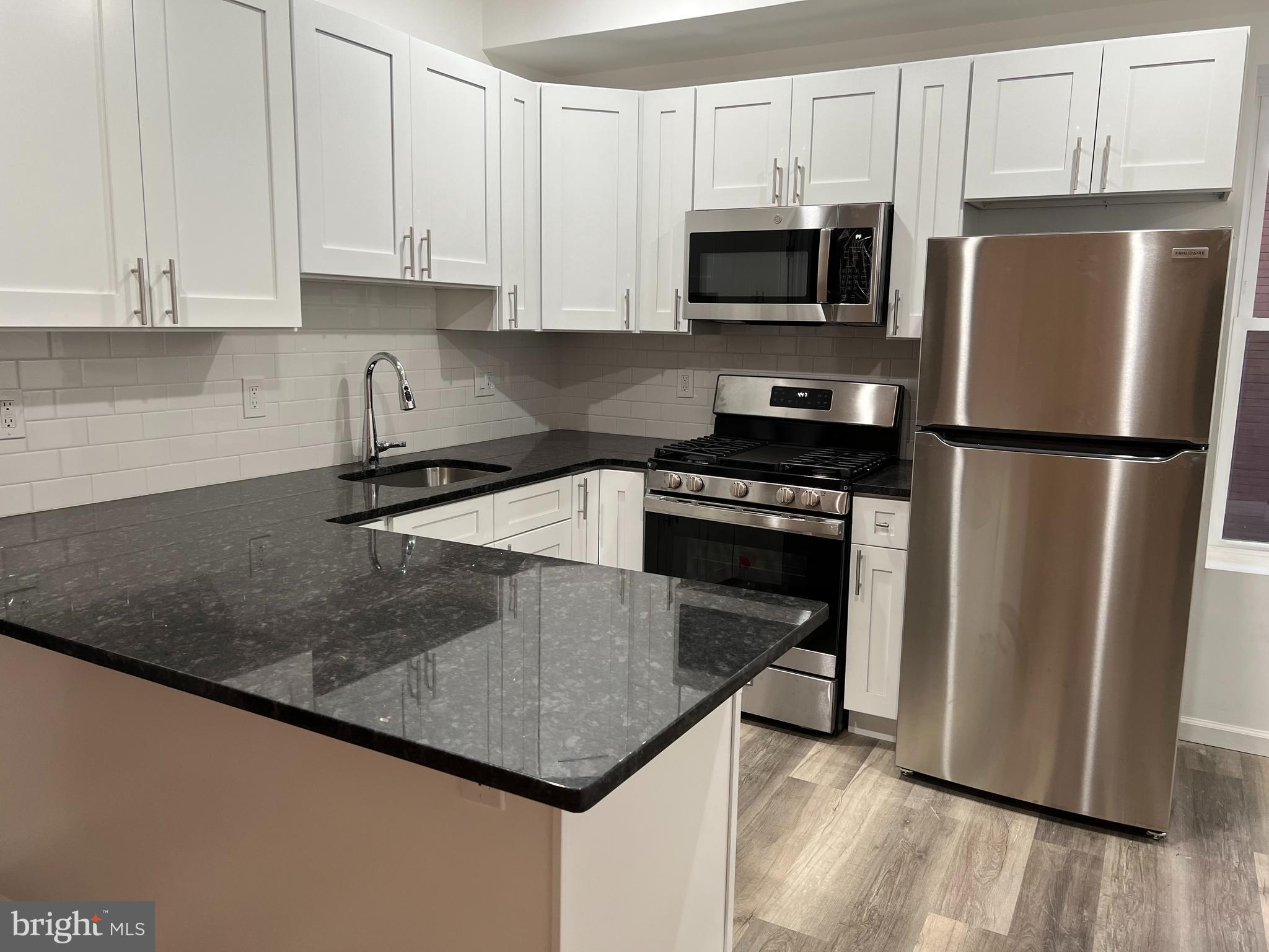2814 Master Street, Unit B Philadelphia, PA 19121 - Photo 6 of 13 a kitchen with granite countertop a refrigerator a sink a stove a microwave and wooden floor