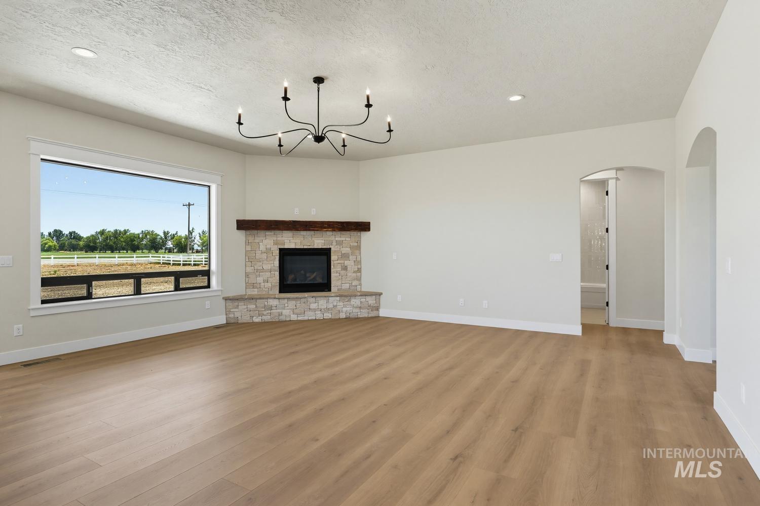 5054 Heritage Drive Marsing, ID 83639 - Photo 14 of 38 Spacious room featuring wood-finish flooring, a contemporary black chandelier, and a stone-clad fireplace with a wood mantel