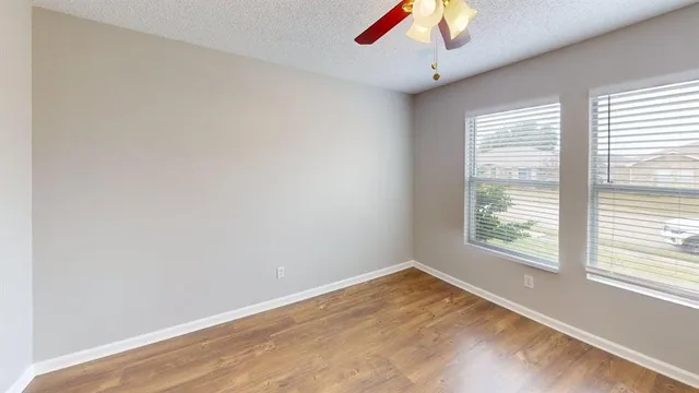 a view of empty room with wooden floor and fan