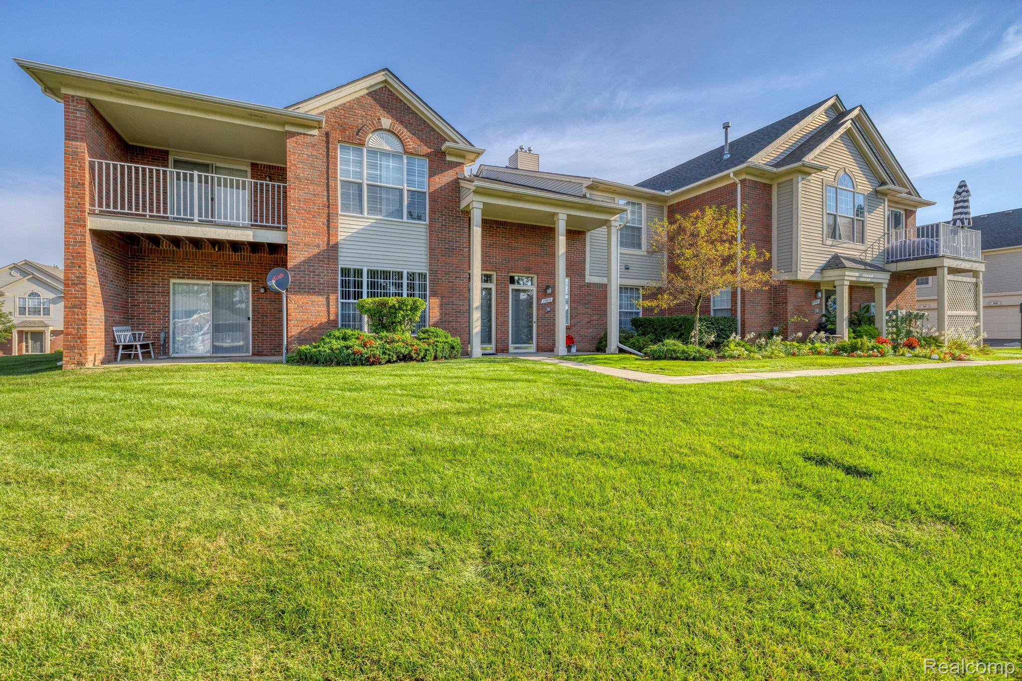 1905 Flagstone Circle Rochester, MI 48307 - Photo 1 of 33 Brick and siding exterior with gabled roof, upper-level balcony, ground-level patio, and surrounding green lawn