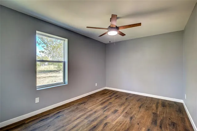 an empty room with wooden floor fan and windows