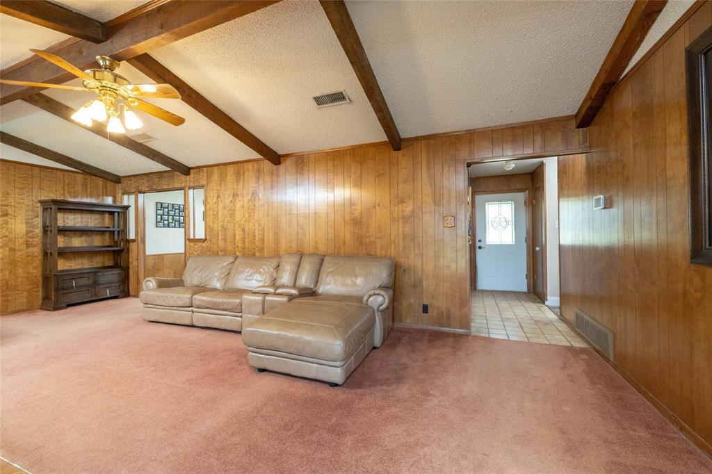 151 County Road 3699 Springtown, TX 76082 - Photo 4 of 35 Spacious living area featuring wood paneling, a vaulted ceiling with exposed wood beams, and a ceiling fan with integrated lighting