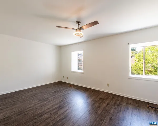 an empty room with wooden floor ceiling fan and windows